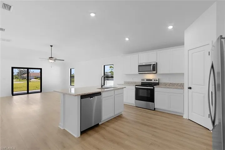 Kitchen featuring stainless steel appliances, light wood-style flooring, an island with sink, white cabinetry, and recessed lighting