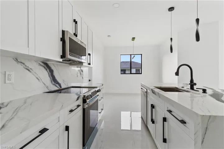 Kitchen featuring light stone countertops, stainless steel appliances, white cabinetry, decorative light fixtures, and tasteful backsplash
