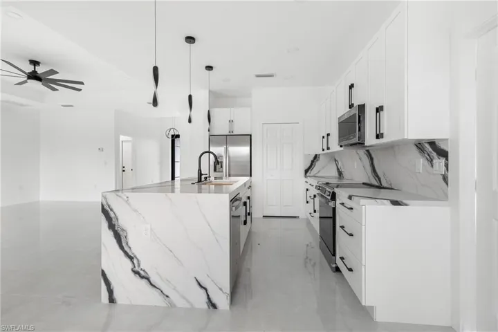 Kitchen with white cabinetry, appliances with stainless steel finishes, pendant lighting, and light stone countertops
