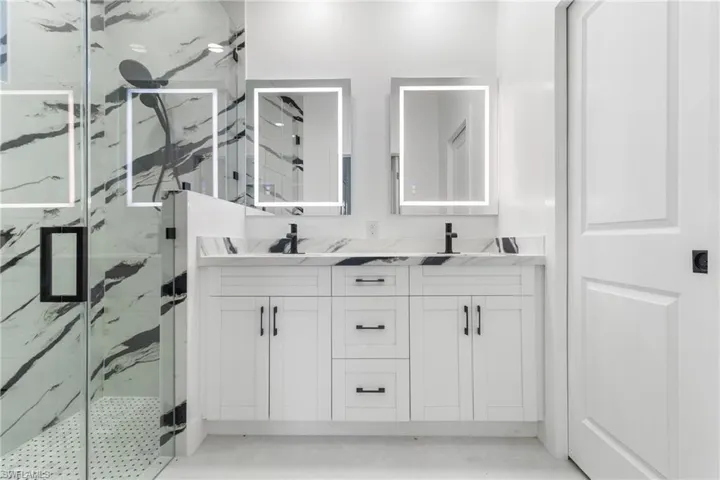 Full bathroom featuring double vanity and a marble finish shower