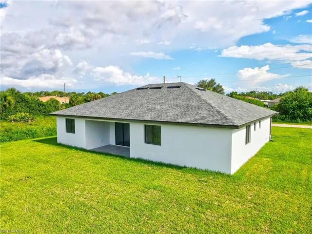 Back of house featuring a lawn, stucco siding, and roof with shingles