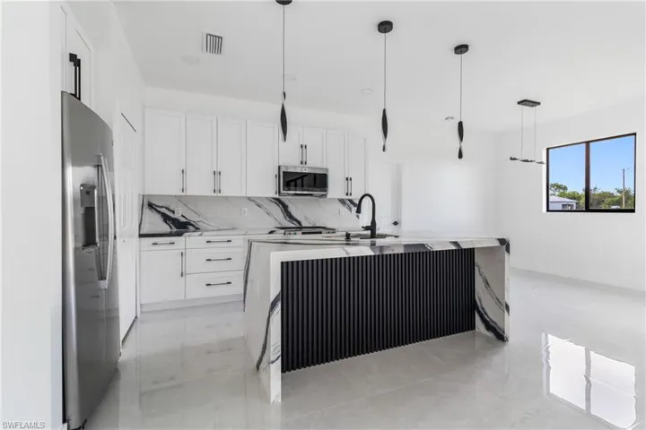 Kitchen with a kitchen island with sink, white cabinetry, decorative light fixtures, and stainless steel appliances