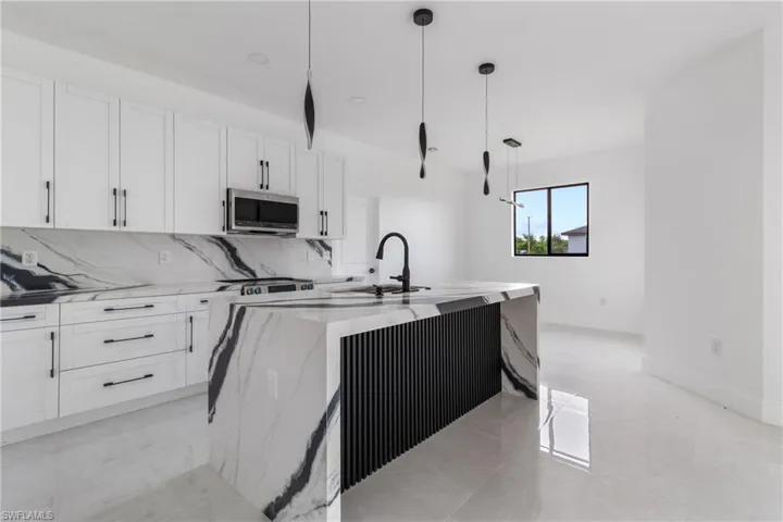Kitchen with light stone countertops, white cabinets, and pendant lighting