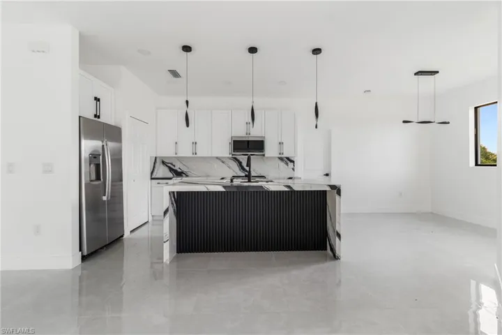 Kitchen with hanging light fixtures, a kitchen island with sink, stainless steel appliances, white cabinetry, and decorative backsplash