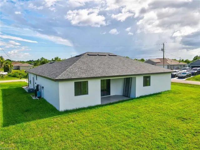 Rear view of property featuring a lawn, roof with shingles, and stucco siding