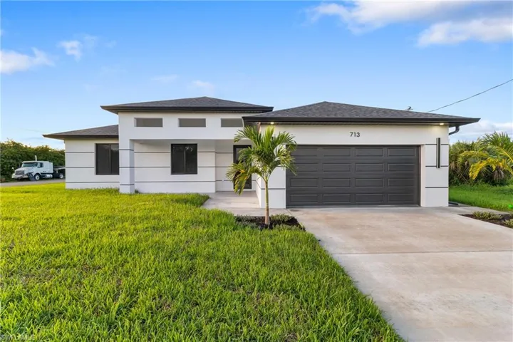 Prairie-style home with concrete driveway, a front yard, stucco siding, an attached garage, and roof with shingles