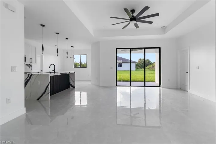 Unfurnished living room with ceiling fan, a tray ceiling, and light marble finish flooring