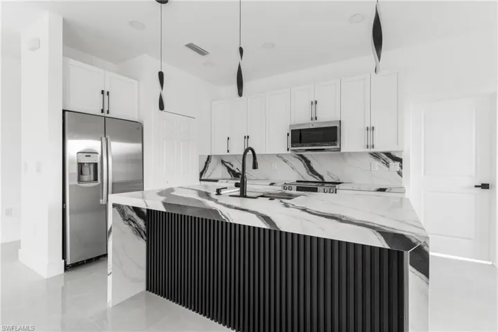 Kitchen with light stone countertops, appliances with stainless steel finishes, and a center island with sink