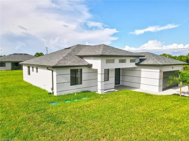 Back of house with a lawn, a shingled roof, a garage, and a patio area