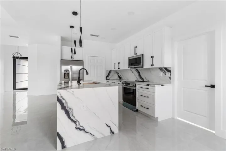 Kitchen with light stone countertops, stainless steel appliances, white cabinetry, and hanging light fixtures