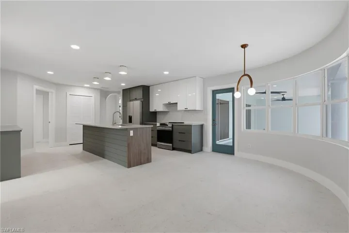Open-concept kitchen and living area featuring a central island with wood-finish paneling, white shaker-style upper cabinetry, and dark lower cabinetry