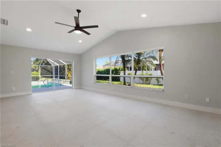 Spacious room featuring vaulted ceilings, recessed lighting, a modern ceiling fan, large windows, and a sliding glass door opening to a screened pool area