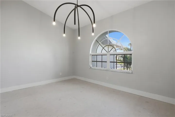 Interior space featuring a contemporary chandelier with curved arms, a large arched window with grid detailing, light-colored walls, white baseboards, and light-toned flooring