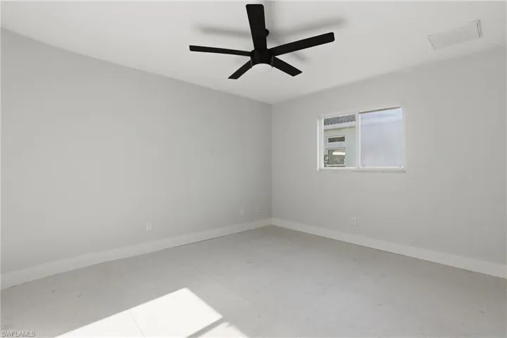 Spacious room featuring light-toned walls, a modern black ceiling fan, white baseboards, and a single window with a white frame