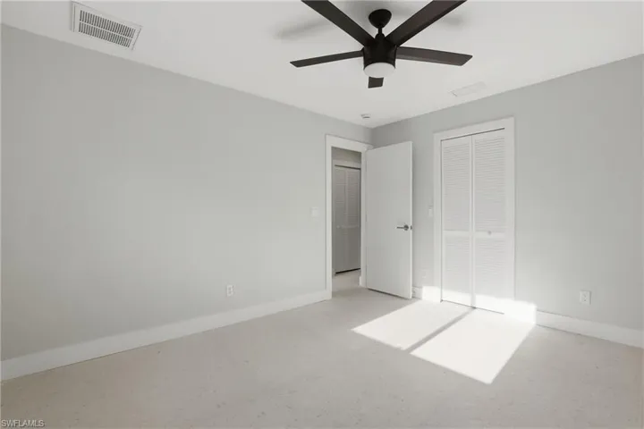 Spacious room featuring light-toned carpeting, neutral wall paint, and a ceiling fan with integrated lighting
