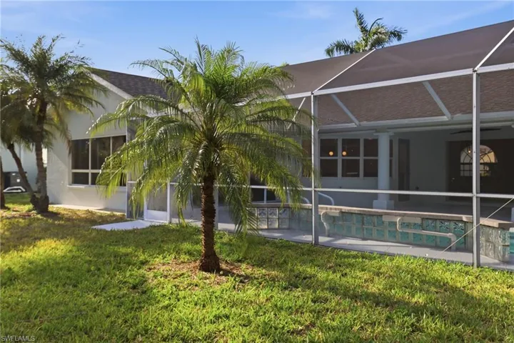 Expansive grass lawn with mature palm trees and a screened-in pool enclosure featuring a pool with glass block detailing