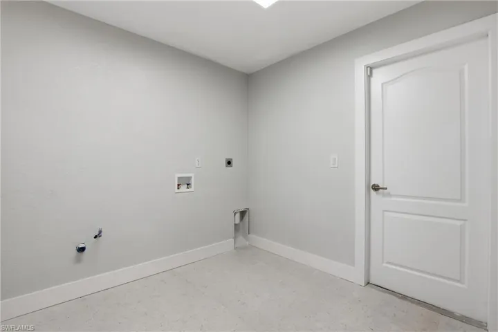 Utility room featuring light gray walls, white baseboards, a white two-panel arched interior door with a brushed nickel handle, and light gray flooring