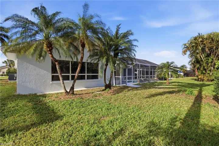Expansive lawn area featuring mature palm trees and a screened-in pool enclosure