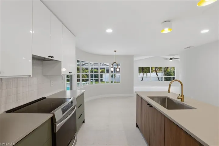 Contemporary kitchen featuring a large island with an undermount sink and brass-finish faucet, a built-in electric range, white upper cabinetry, and a textured tile backsplash