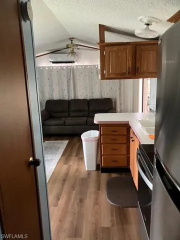 Kitchen featuring vaulted ceiling, ceiling fan, range, refrigerator, and dark wood-type flooring