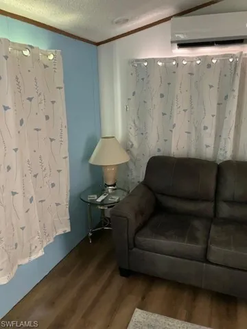 Living room with wood-type flooring, a textured ceiling, an AC wall unit, and crown molding