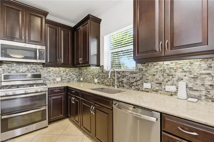Kitchen with appliances with stainless steel finishes, dark brown cabinetry, crown molding, light stone counters, and light tile patterned flooring