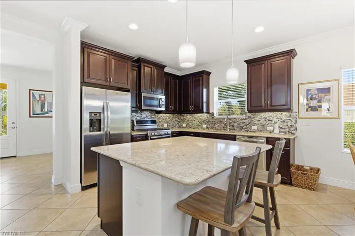 Kitchen with crown molding, dark brown cabinets, a breakfast bar area, stainless steel appliances, and a kitchen island