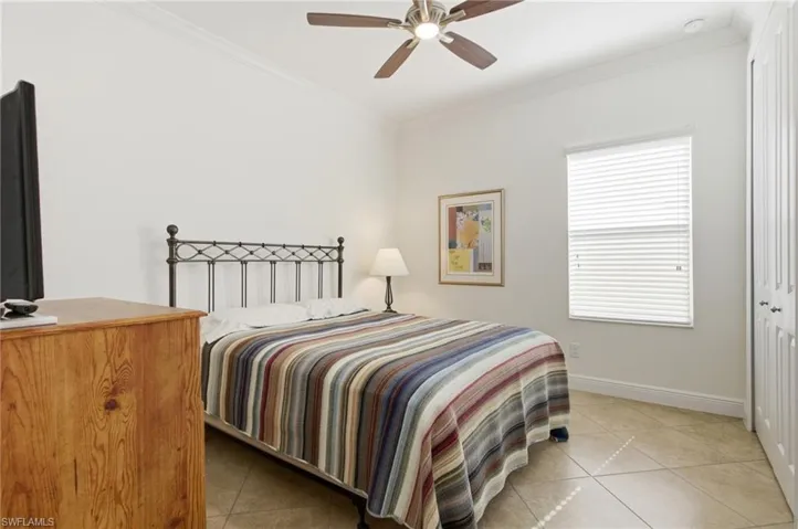 Bedroom with crown molding, light tile patterned flooring, a ceiling fan, and a closet
