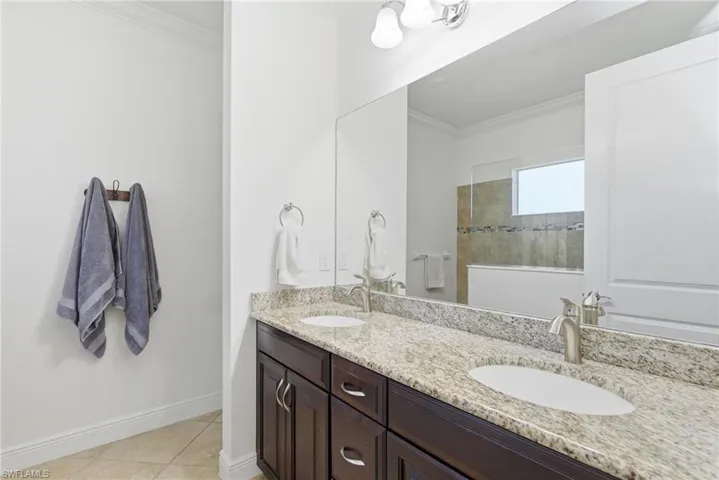 Full bath featuring ornamental molding, double vanity, light tile patterned floors, and a walk in shower