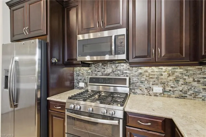 Kitchen featuring stainless steel appliances, dark brown cabinets, light stone counters, and decorative backsplash