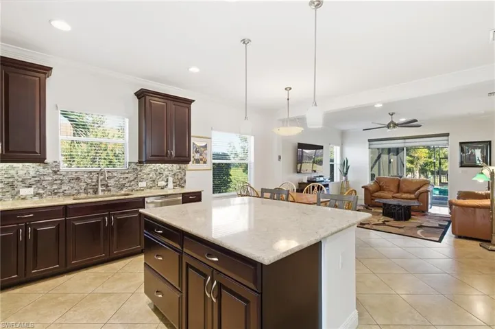 Kitchen featuring dark brown cabinets, decorative backsplash, light stone counters, hanging light fixtures, and recessed lighting