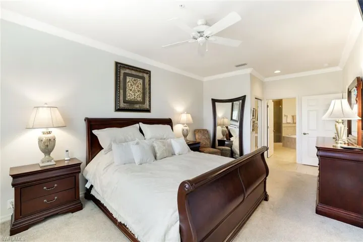 Bedroom with ornamental molding, ensuite bathroom, light colored carpet, and a ceiling fan