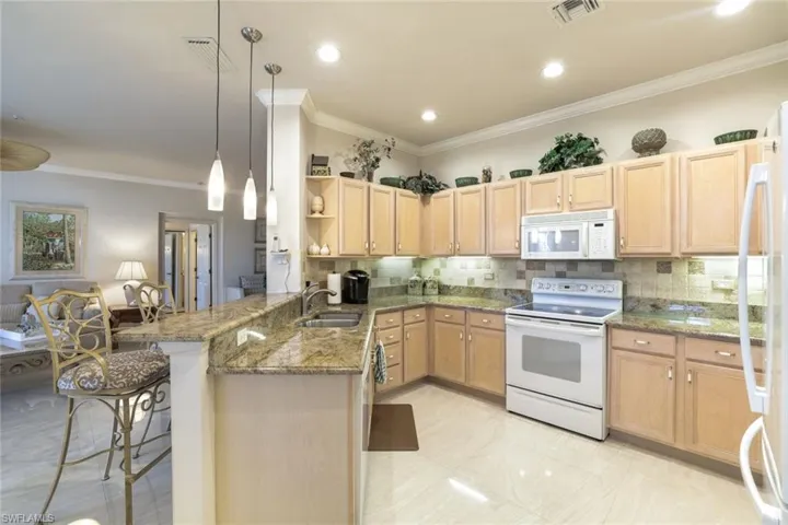 Kitchen featuring a peninsula, white appliances, ornamental molding, a kitchen bar, and light wood finish cabinetry