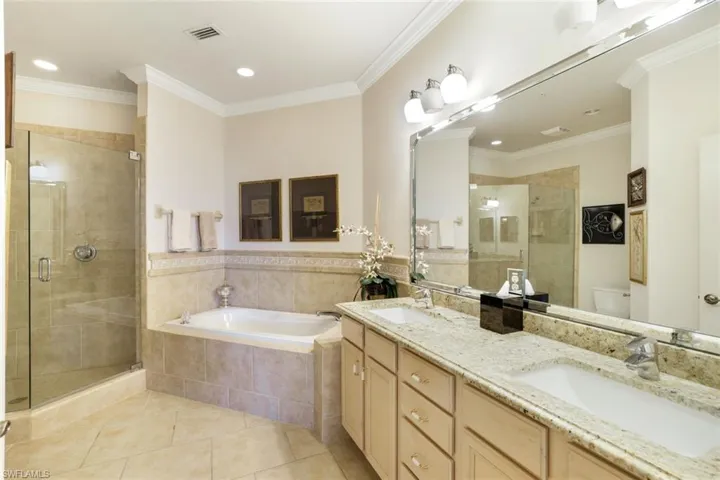 Full bath with ornamental molding, double vanity, a shower stall, light tile patterned floors, and a garden tub