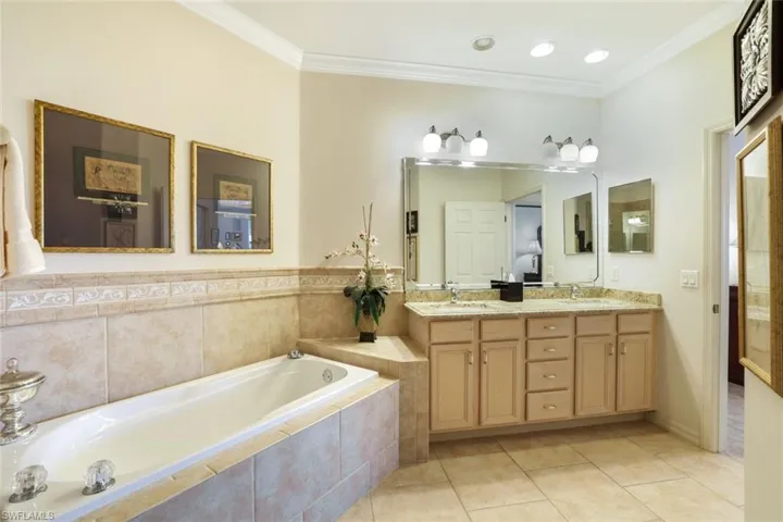 Bathroom featuring double vanity, ornamental molding, light tile patterned floors, and a garden tub