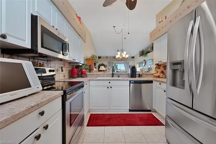 Kitchen with appliances with stainless steel finishes, vaulted ceiling, backsplash, a chandelier, and light tile patterned flooring
