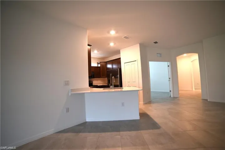 Kitchen featuring arched walkways, dark brown cabinetry, a peninsula, high end refrigerator, and light tile patterned floors