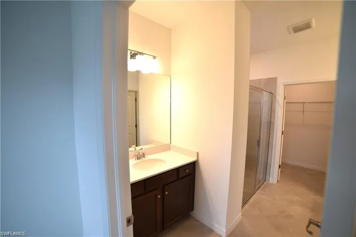 Bathroom featuring a walk in closet, a shower stall, light tile patterned floors, and vanity