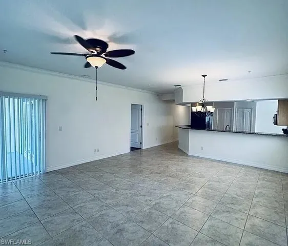 Open-concept living area featuring tile flooring, ceiling fan with integrated lighting, and a kitchen pass-through with a built-in counter