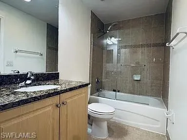 Master Bedroom Bathroom featuring a vanity with a dark speckled countertop, light wood-finish cabinetry, a built-in sink, and a combination shower/tub with a tiled surround and glass enclosure