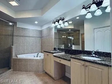 Master Bedroom Dual vanity with granite countertops, integrated sinks, a built-in jetted tub, a glass-enclosed shower, and tiled walls and flooring