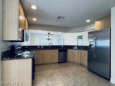 Kitchen featuring light wood-finish cabinetry, dark stone countertops, stainless steel appliances, and tile flooring