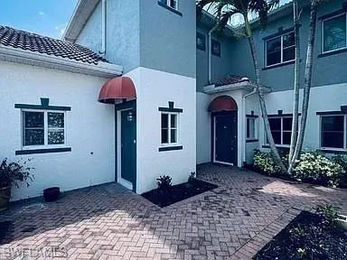 Stucco exterior with contrasting trim, brick paver courtyard, and red fabric awnings