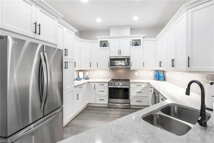 Kitchen featuring stainless steel appliances, white cabinets, backsplash, light stone counters, and recessed lighting