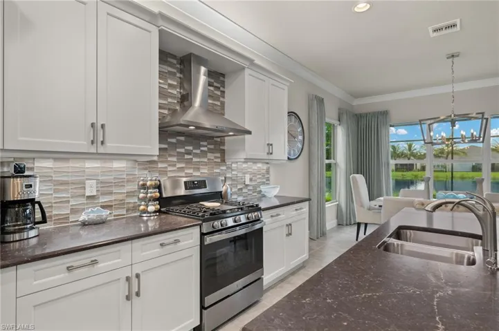 Kitchen featuring pendant lighting, soft tone backsplash, sink, wall chimney exhaust hood, and gas range