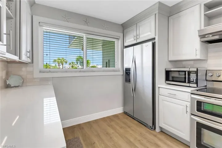 Kitchen featuring light hardwood / wood-style floors, stainless steel appliances, backsplash, custom exhaust hood, and white cabinetry