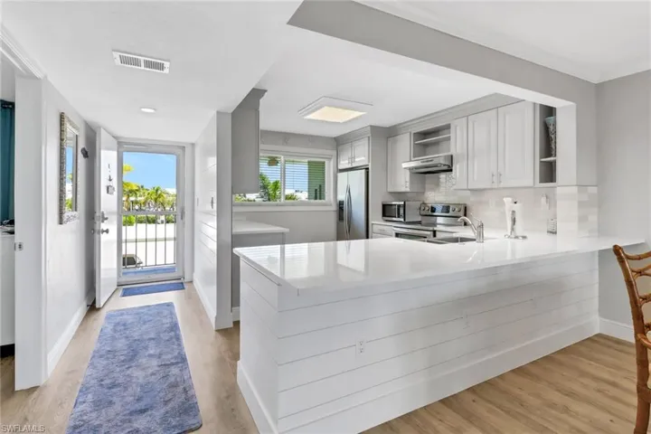 Kitchen with appliances with stainless steel finishes, light hardwood / wood-style floors, backsplash, and kitchen peninsula