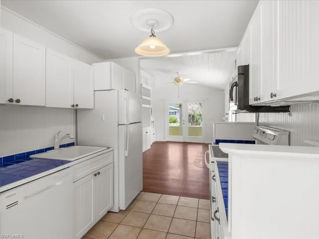 Kitchen featuring white dishwasher, light wood-type flooring, pendant lighting, sink, and vaulted ceiling