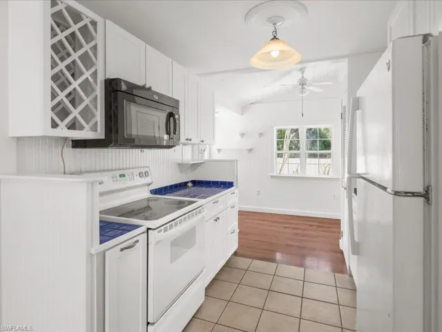 Kitchen with white appliances, light wood-type flooring, pendant lighting, backsplash, and white cabinetry
