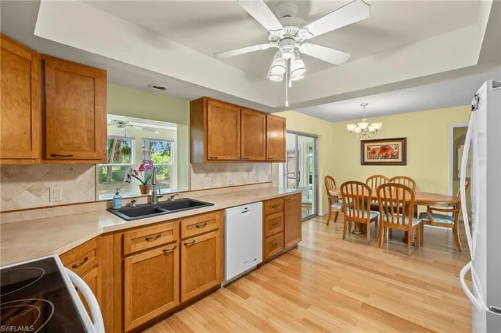 Kitchen with white appliances, light wood-type flooring, ceiling fan with notable chandelier, backsplash, and decorative light fixtures